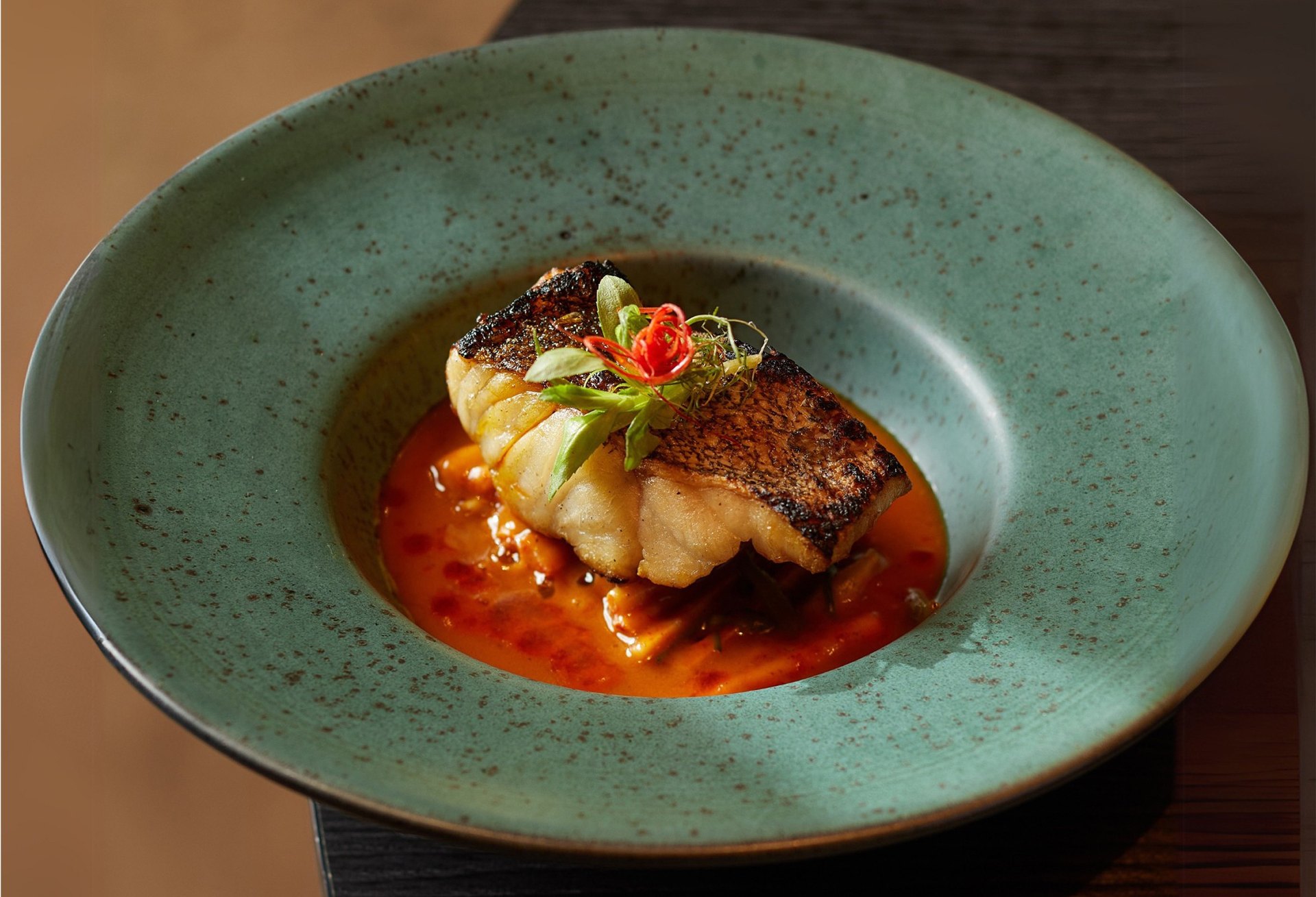 A fillet of fish in a red sauce, served in a speckled green bowl at Vien Dining